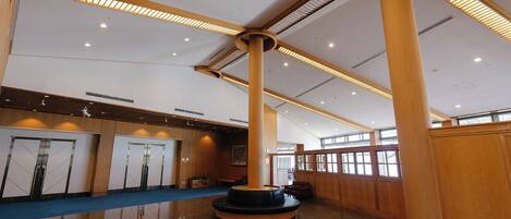 A spacious lobby with a central column, a blue carpet, and wooden paneling.