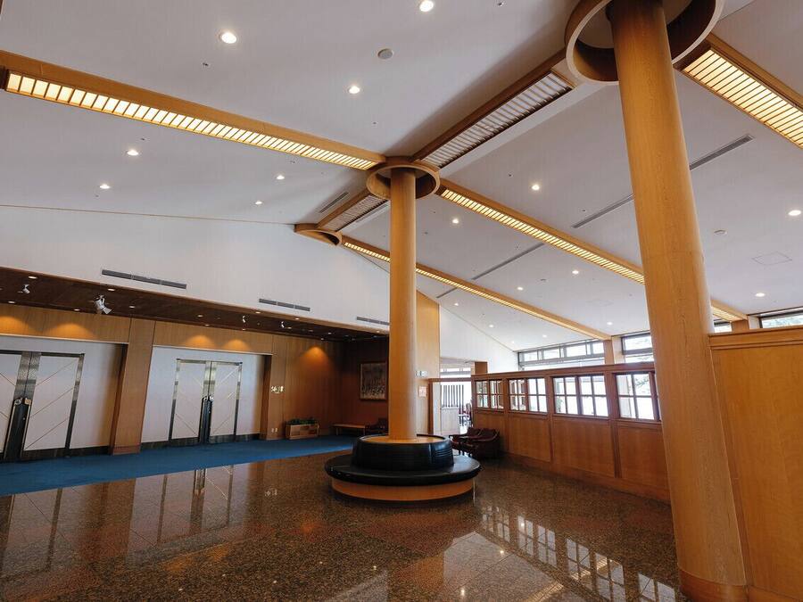 A spacious lobby with a central column, a blue carpet, and wooden paneling.