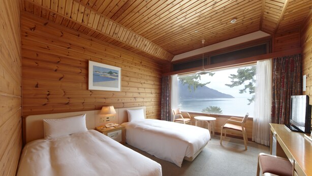 A wooden cabin room with two beds, a desk, a chair, and a window overlooking a body of water. - Okubiwako Makino Grand Park Hotel (Takashima)