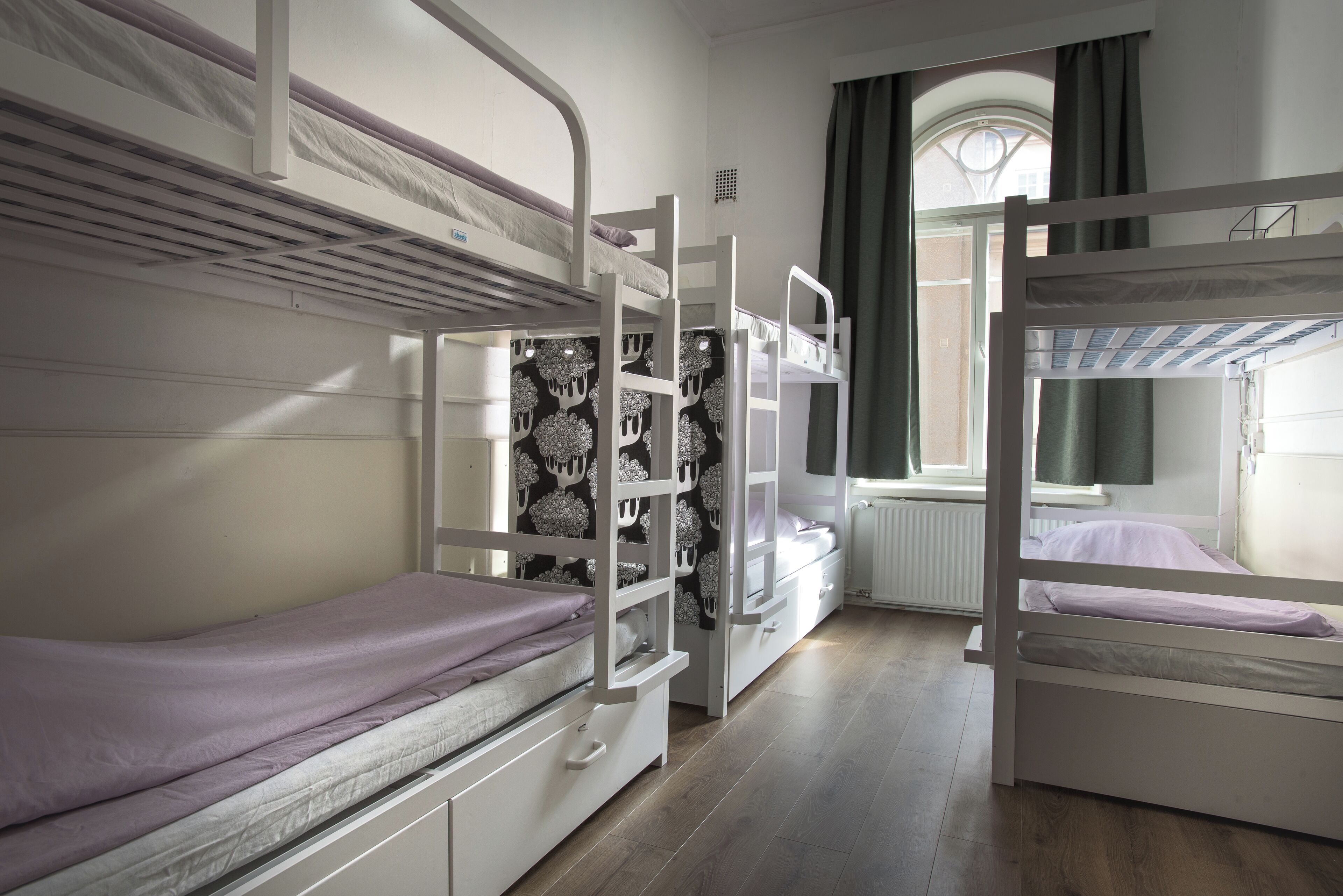 A bunk bed room with a window, a radiator, and a curtain.