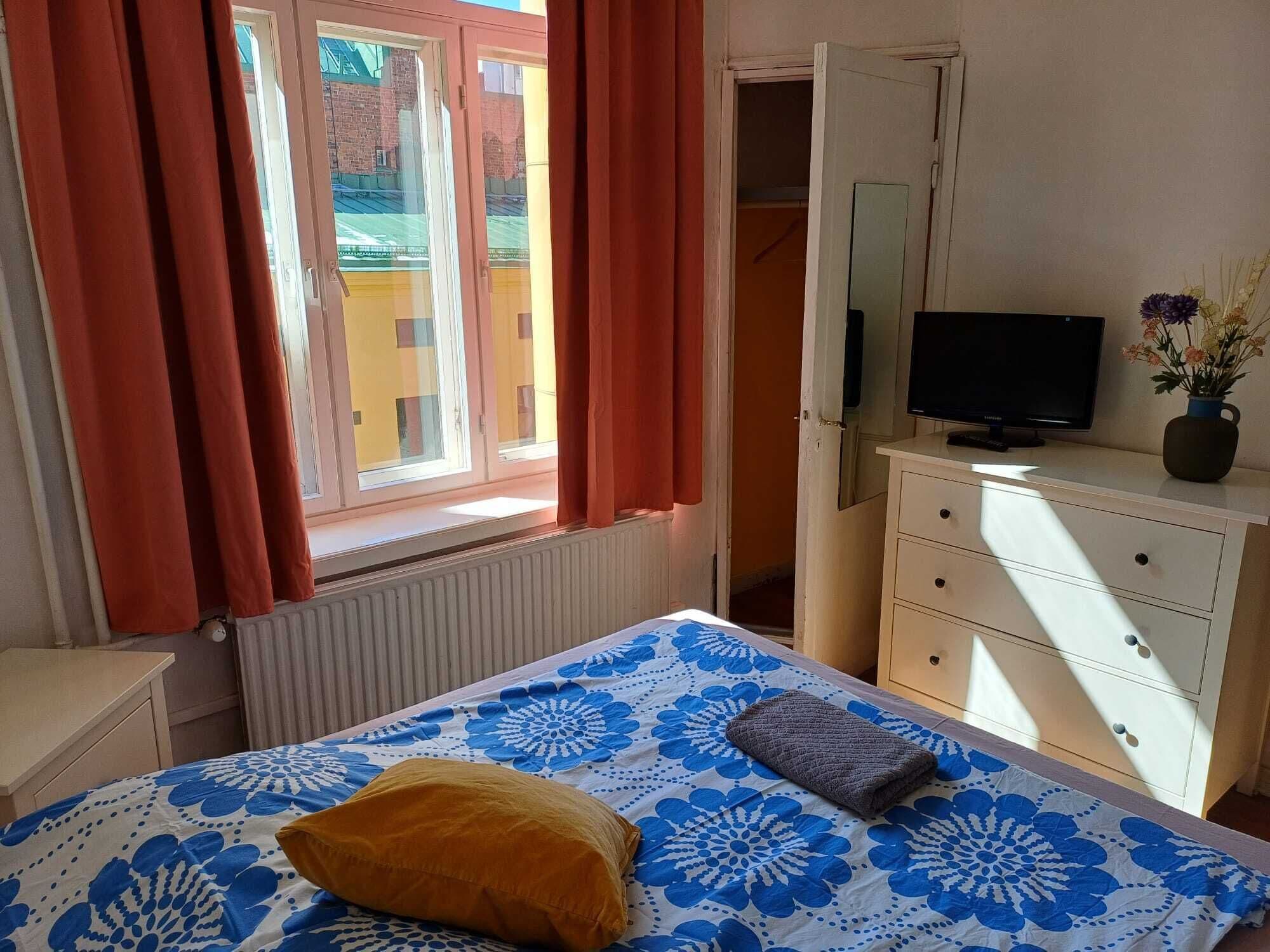 Un dormitorio con cama, cómoda, televisor y ventana con cortinas.