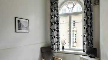 A bedroom with a bed, a desk, a chair, a window with curtains, and a picture on the wall.
