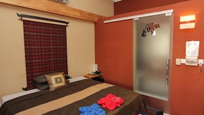 A hotel room with a bed, a wooden headboard, an air conditioning unit, a red curtain, a door with a sign, a bedside table with a lamp, and a checkered floor. - The Local Riverside (Phnom Penh)