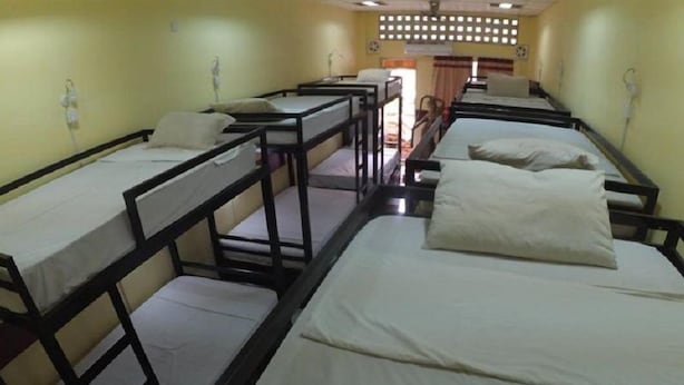 A dormitory room with bunk beds, a small window, and a door. - The Local Riverside (Phnom Penh)
