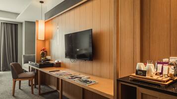 Une chambre d’hôtel avec un mur lambrissé en bois, un téléviseur à écran plat fixé au-dessus d’un bureau en bois, une chaise, un porte-revues et un coin café.
