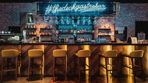 A bar area with a neon sign reading "The Deck Gastrobav," bar stools, and shelves stocked with bottles and glasses. - WEIL Hotel (Ipoh)