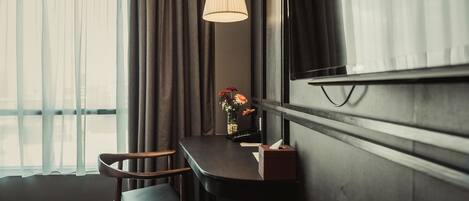 A hotel room with a desk, chair, lamp, and a vase with flowers.
