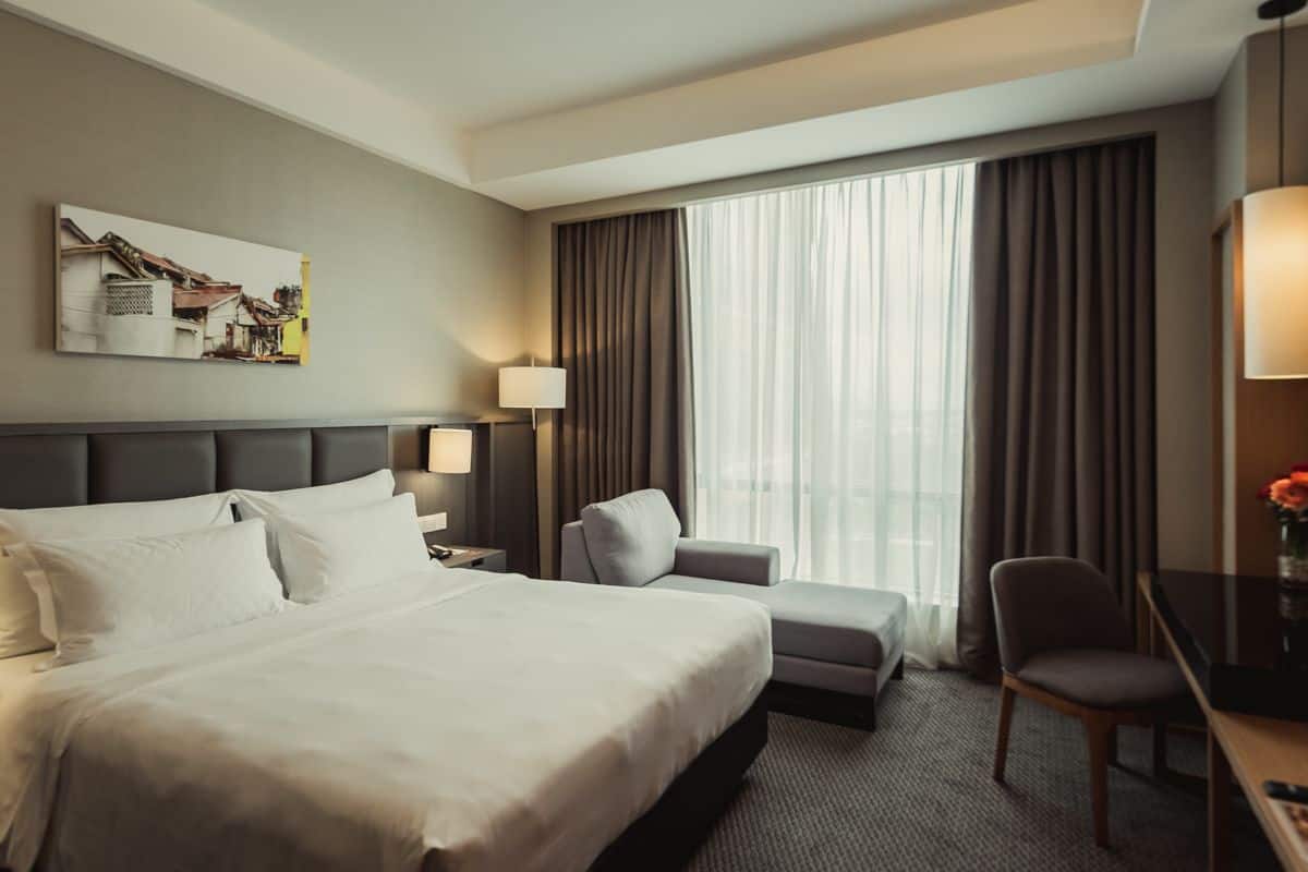 A hotel room with a large bed, a desk, a chair, a lamp, and a window with curtains.