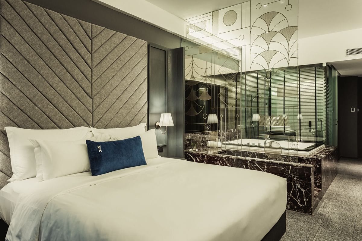 A modern hotel room with a large bed, a marble bathroom, and a decorative wall.