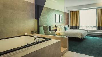 Habitació d'hotel moderna amb una banyera gran, un sofà, un llit i una finestra àmplia amb cortines.