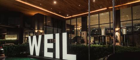 Un edificio moderno con un llamativo letrero 'WEIL', amplias ventanas y un interior bien iluminado.