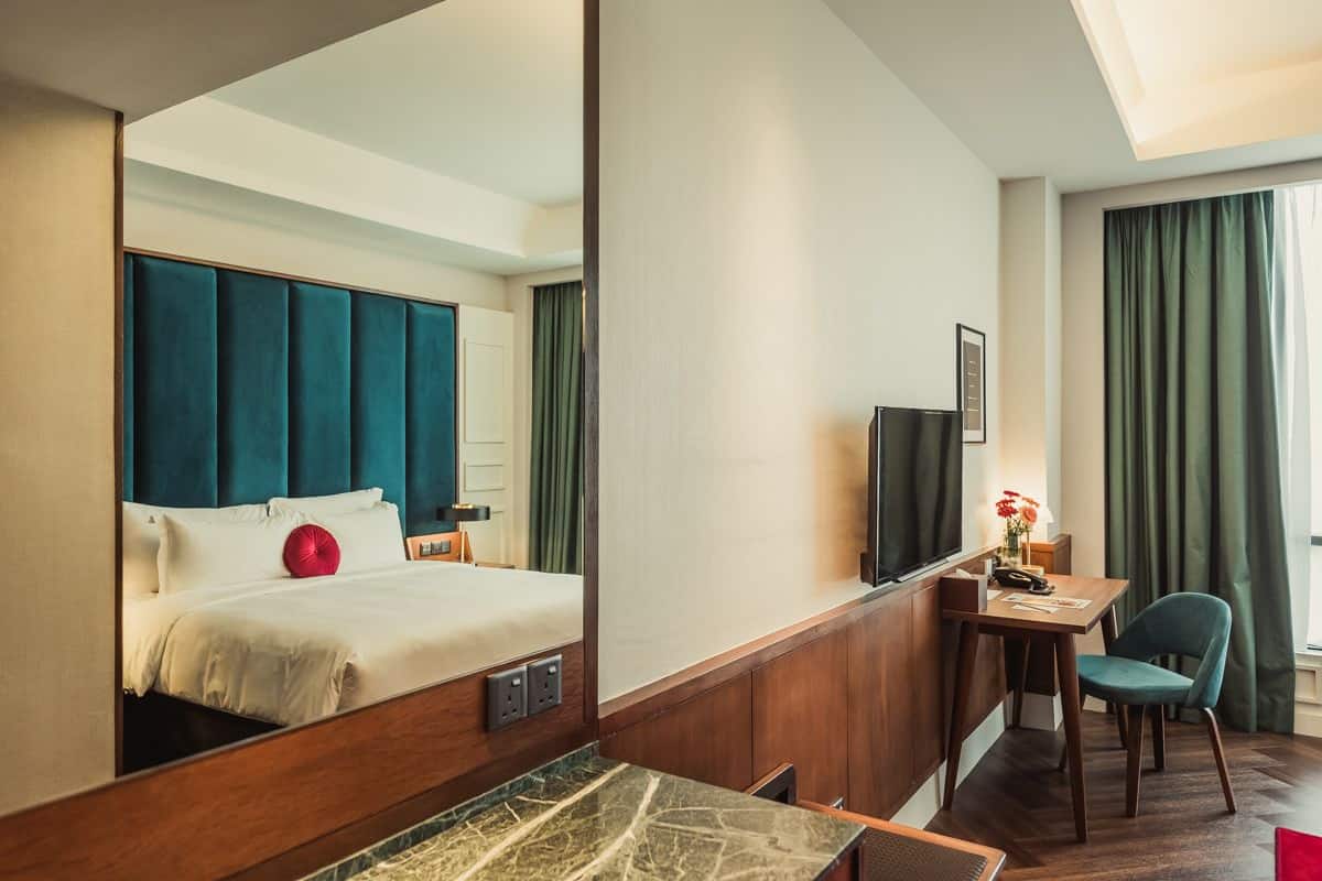 A hotel room with a bed, a desk, a chair, a television, and a window with curtains.