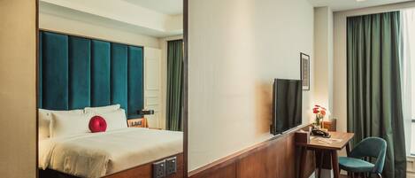 A hotel room with a bed, a desk, a chair, a television, and a window with curtains.