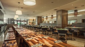 A modern restaurant with long wooden tables, multiple seating areas, and pendant lighting. - WEIL Hotel (Ipoh)