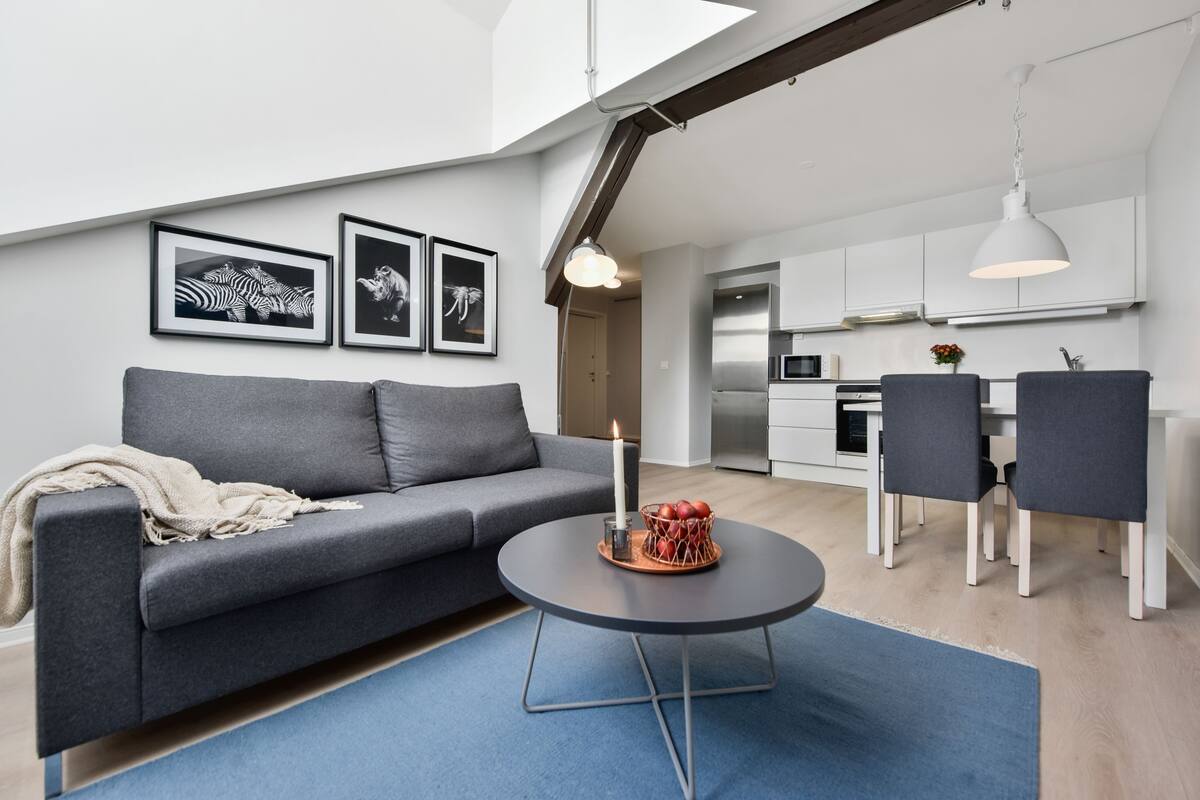 A modern living room with a grey sofa, a round coffee table with a candle, and framed artwork on the wall.