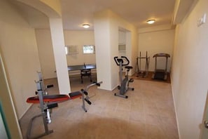 Ein Heimfitnessraum mit Langhantelbank, Crosstrainer und Laufbändern.