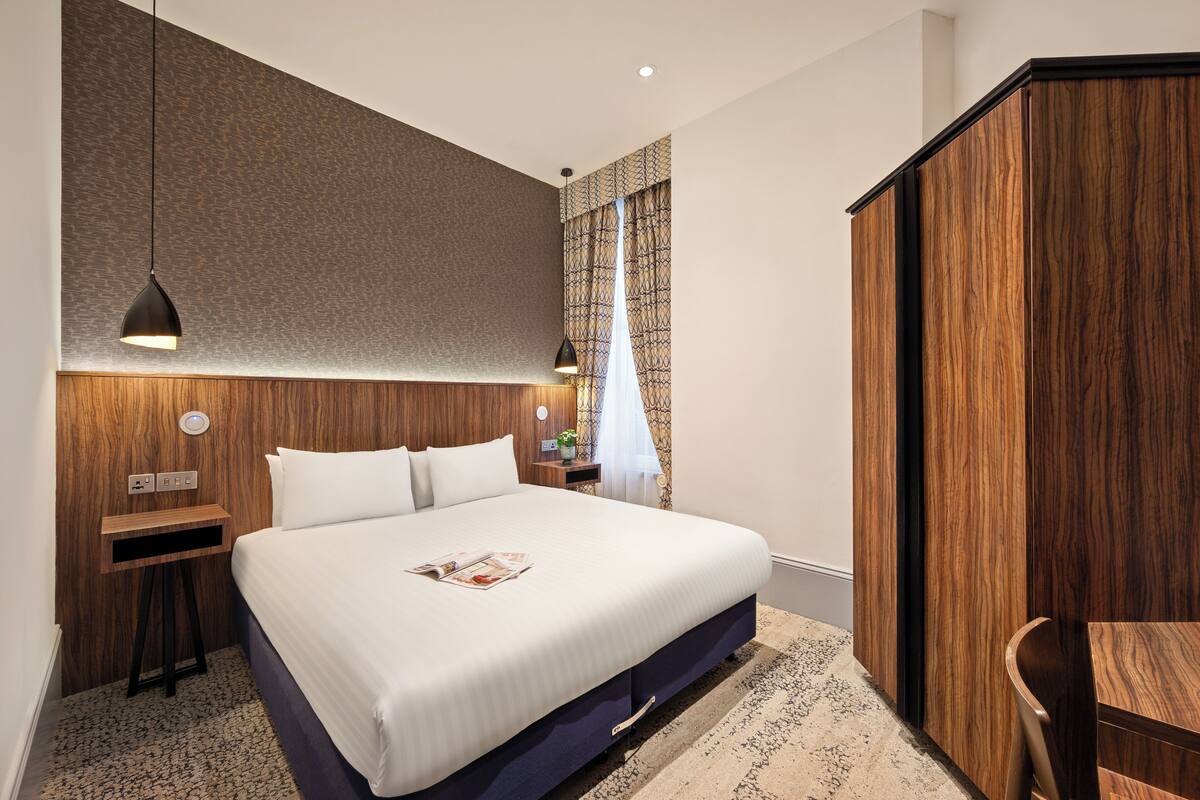 Een moderne hotelkamer met een groot bed, een houten hoofdbord, nachtkastjes en een kledingkast.
