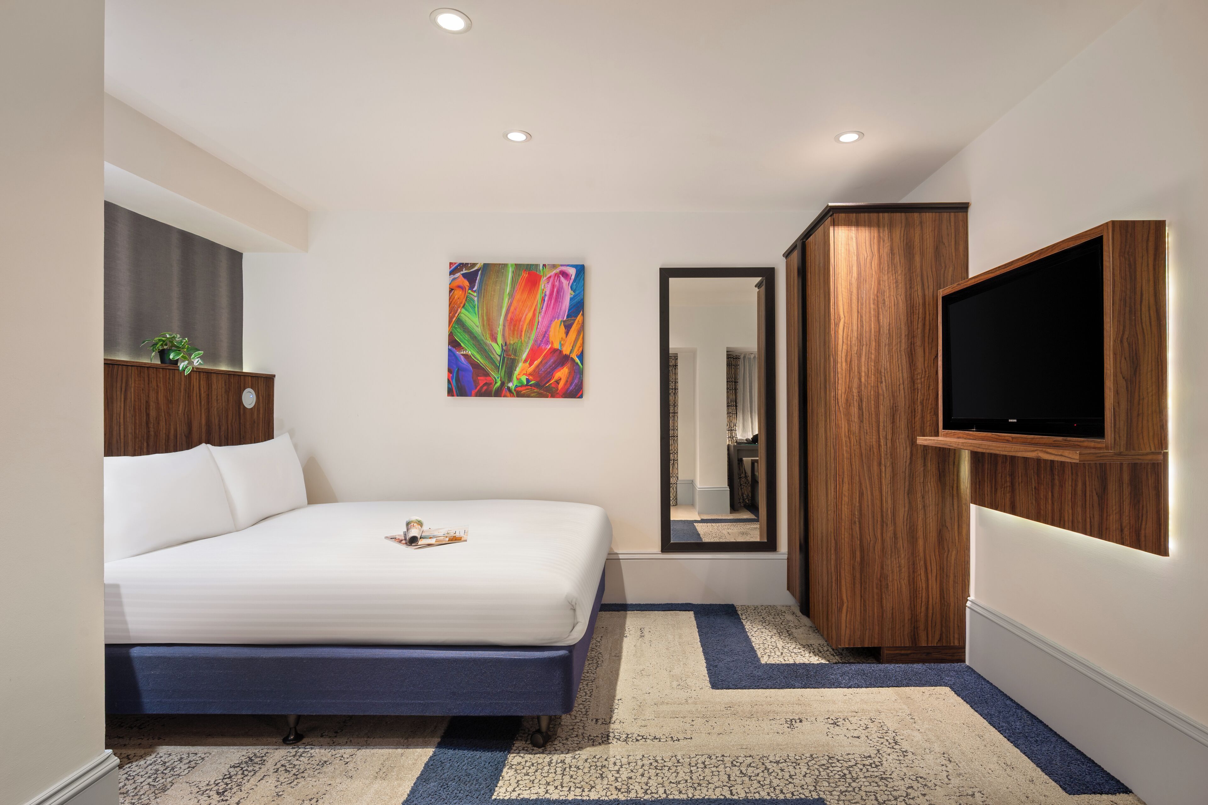 A bedroom with a bed, a TV, a mirror, and a painting on the wall.