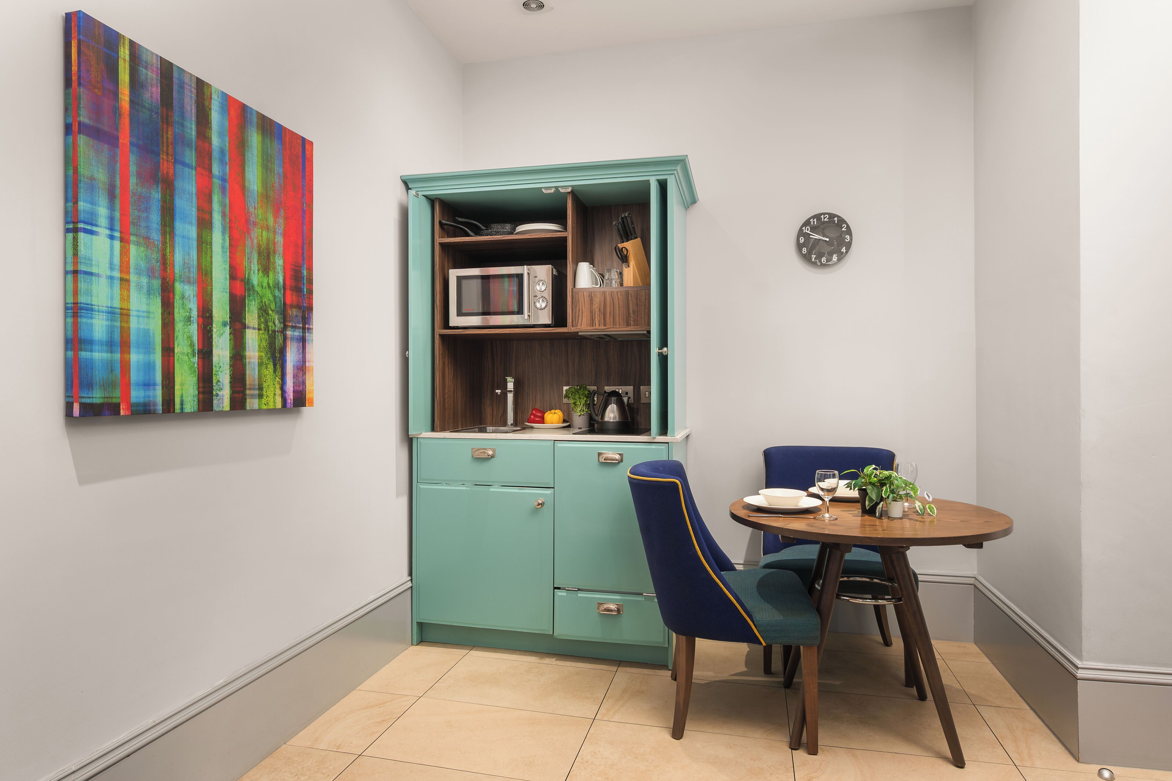 A compact kitchen with a teal cabinet, a microwave, and a clock on the wall.