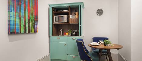A compact kitchen with a teal cabinet, a microwave, and a clock on the wall.
