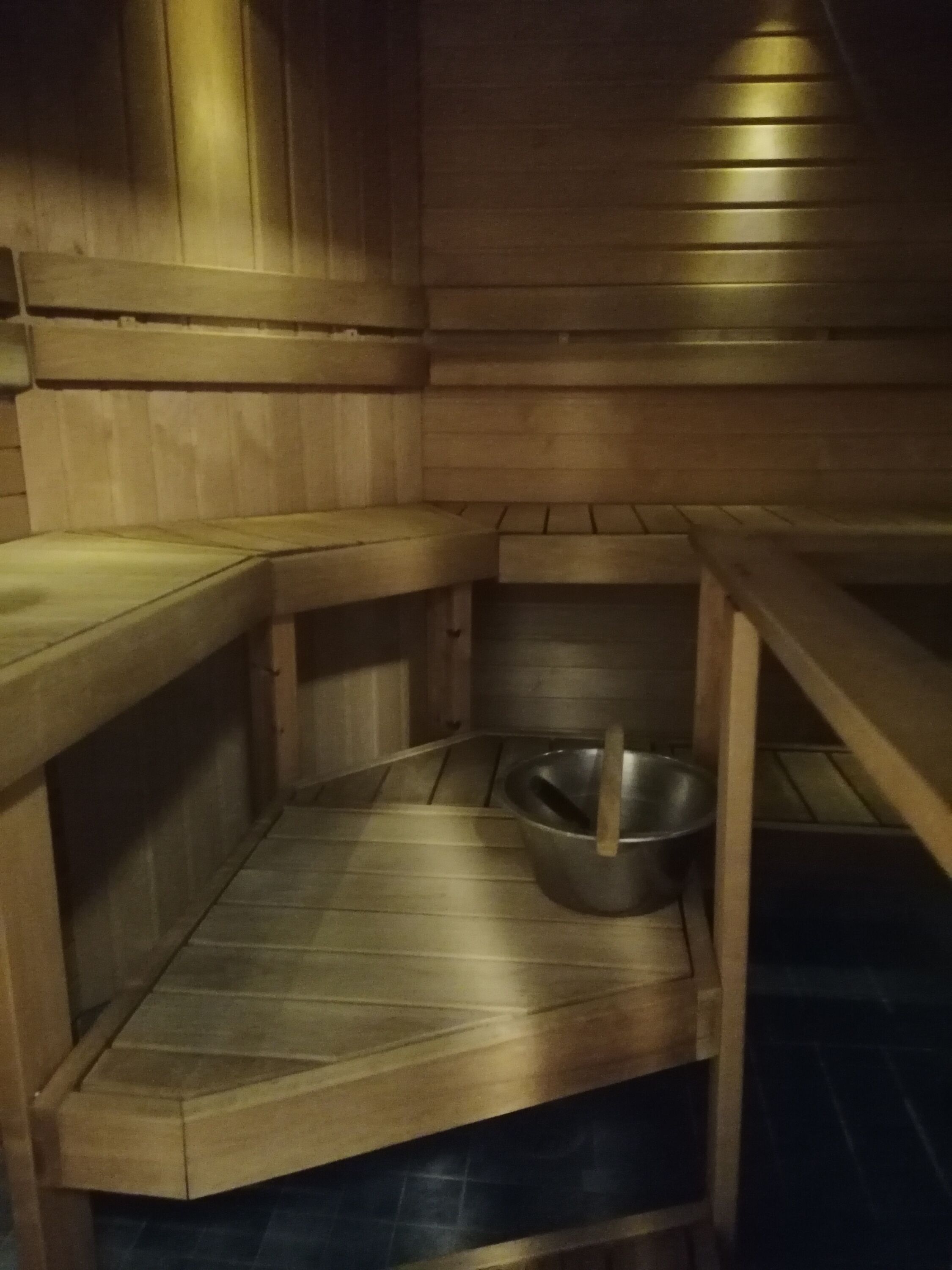 A wooden interior with a bench, a metal bowl, and a wooden table.