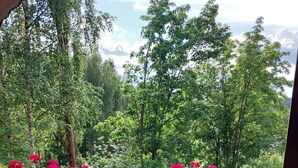 Een houten terras met een leuning, met uitzicht op een tuin met rode bloemen en groene bomen.