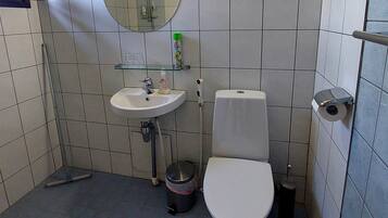 A small, tiled bathroom with a white sink, mirror, toilet, and a trash bin.