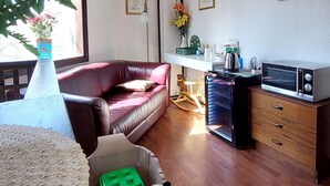 Een woonkamer met een houten vloer, een rode bank, een witte fauteuil, een salontafel, een tv-meubel met een magnetron, en een klein hondenbed met twee honden.