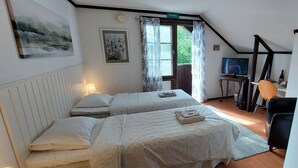 Een slaapkamer met twee bedden, een bureau met stoel, een televisie en een raam met gordijnen.