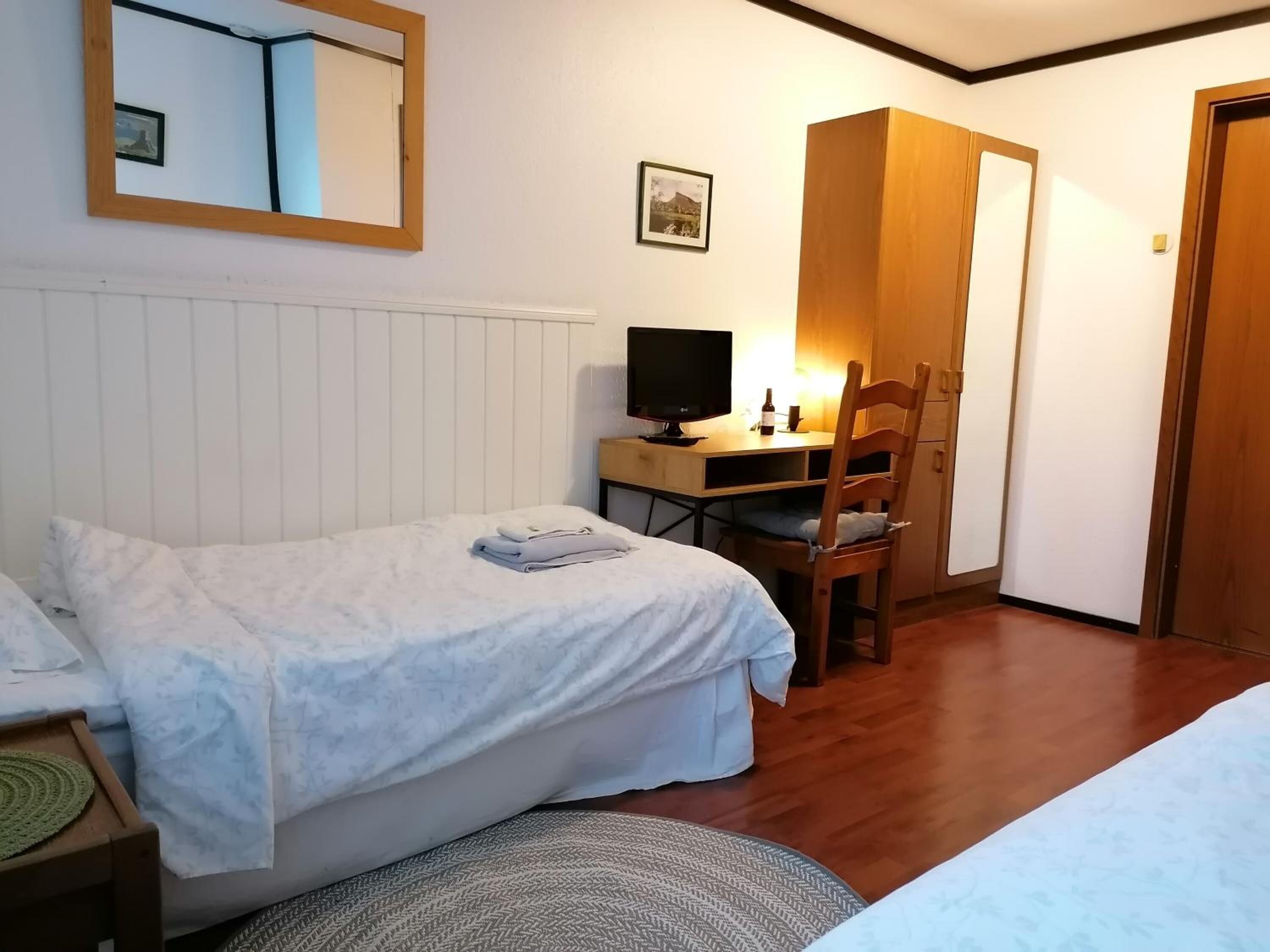 Una camera da letto con un letto, una scrivania con un computer, una sedia e un armadio in legno.
