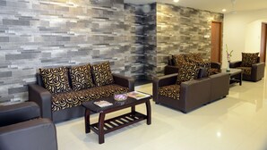A modern living room with two sofas and a coffee table, a stone-patterned wall, and a door in the background. - De Castle Inn (Chennai)