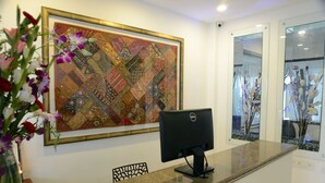 A reception desk with a computer, a large framed artwork, and a vase with flowers. - De Castle Inn (Chennai)