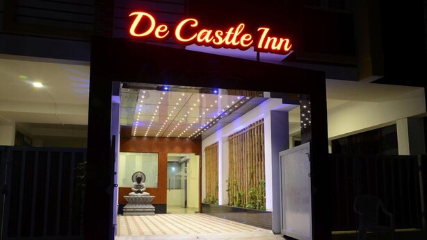 The entrance of De Castle Inn with a neon sign, a statue, and a modern interior visible through the doorway. - De Castle Inn (Chennai)