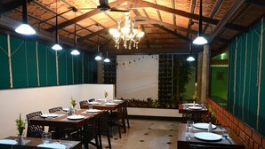 A restaurant with wooden tables and chairs, a chandelier, and green walls. - De Castle Inn (Chennai)