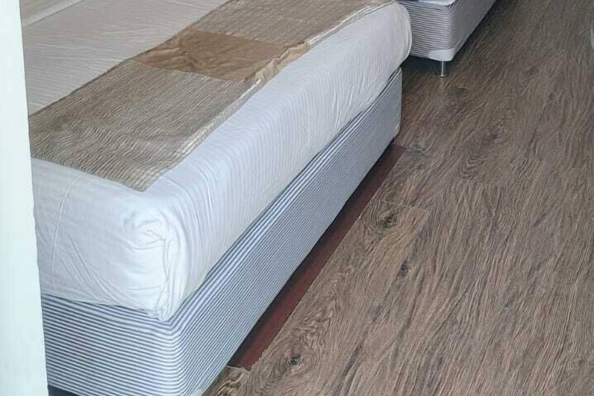 A hotel room with two beds, wooden flooring, a ceiling fan, and wall-mounted air conditioning.