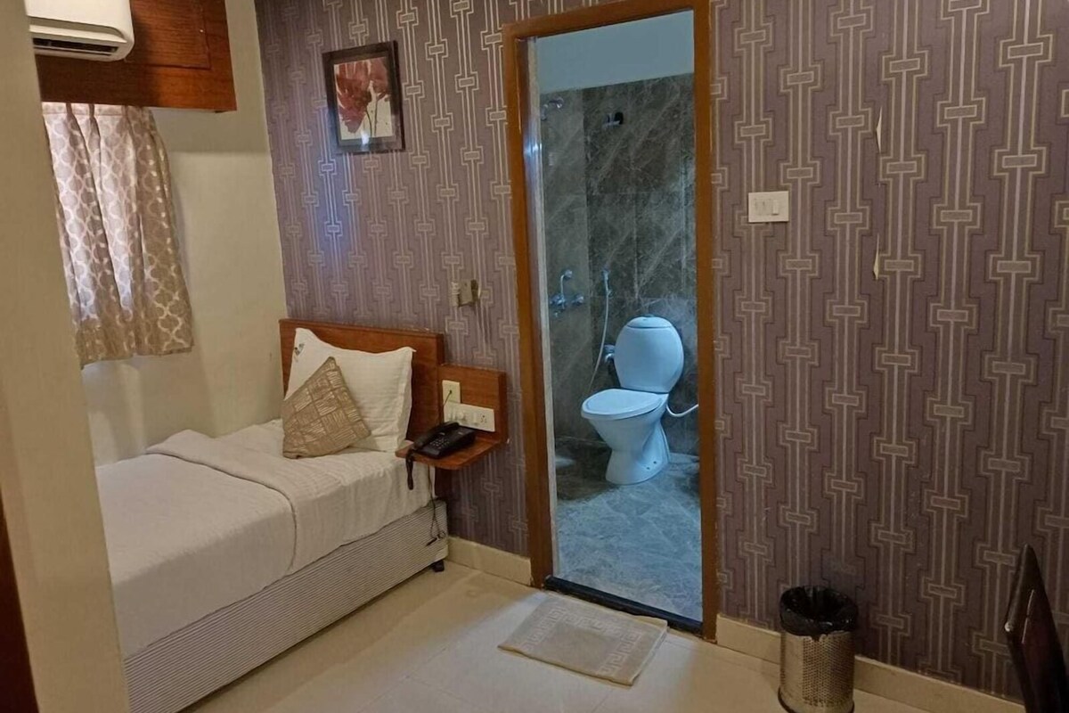 A bedroom with a bed, bedside table, and a door leading to a bathroom with a toilet and shower.