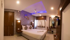A modern hotel room with a large bed, a wardrobe, a vanity with a mirror, and a small seating area. - De Castle Inn (Chennai)