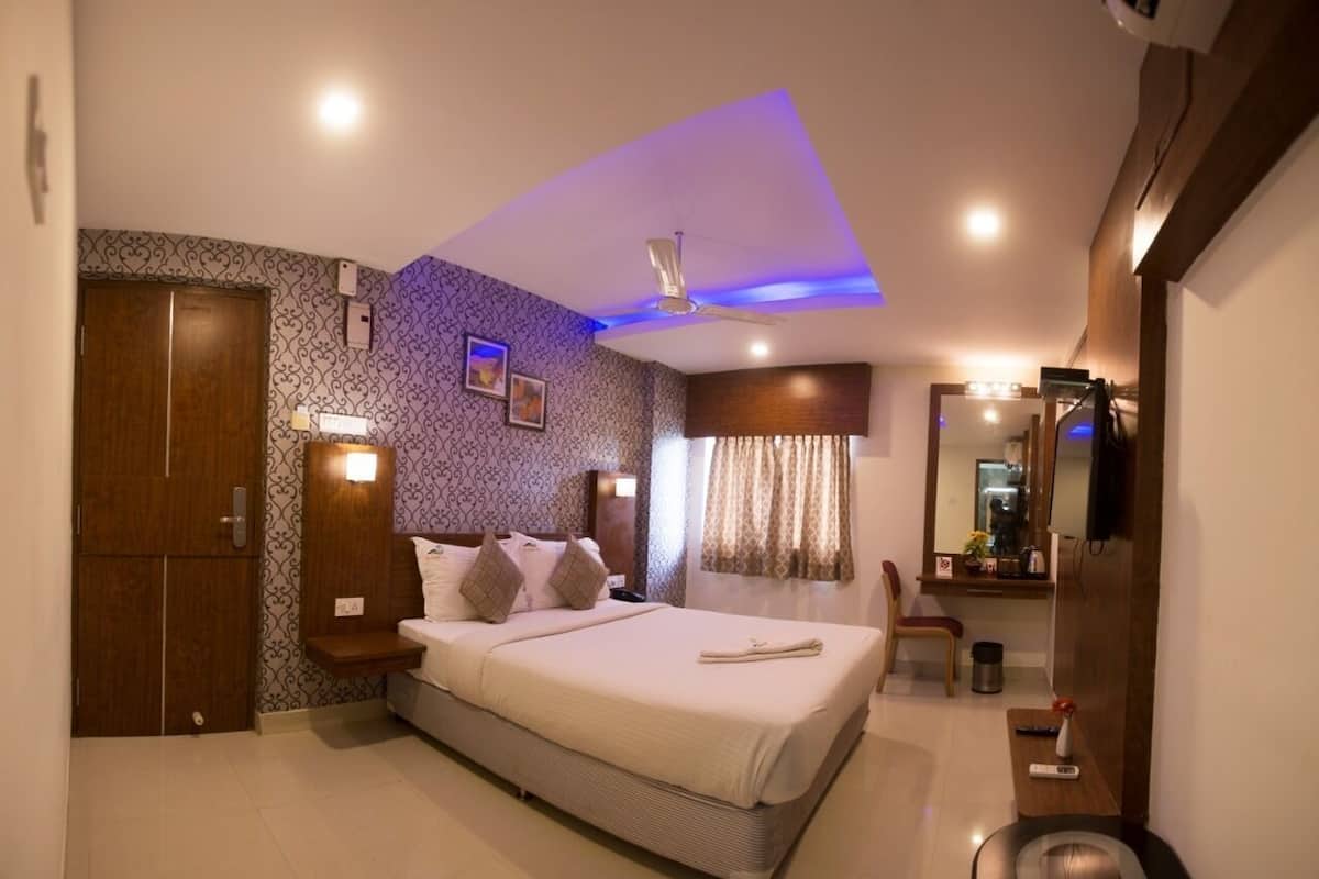 A modern hotel room with a large bed, a wardrobe, a vanity with a mirror, and a small seating area.