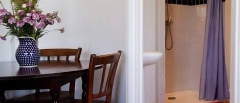 Una habitación con una mesa de comedor de madera y sillas, un florero con flores y un área de ducha con cortina.
