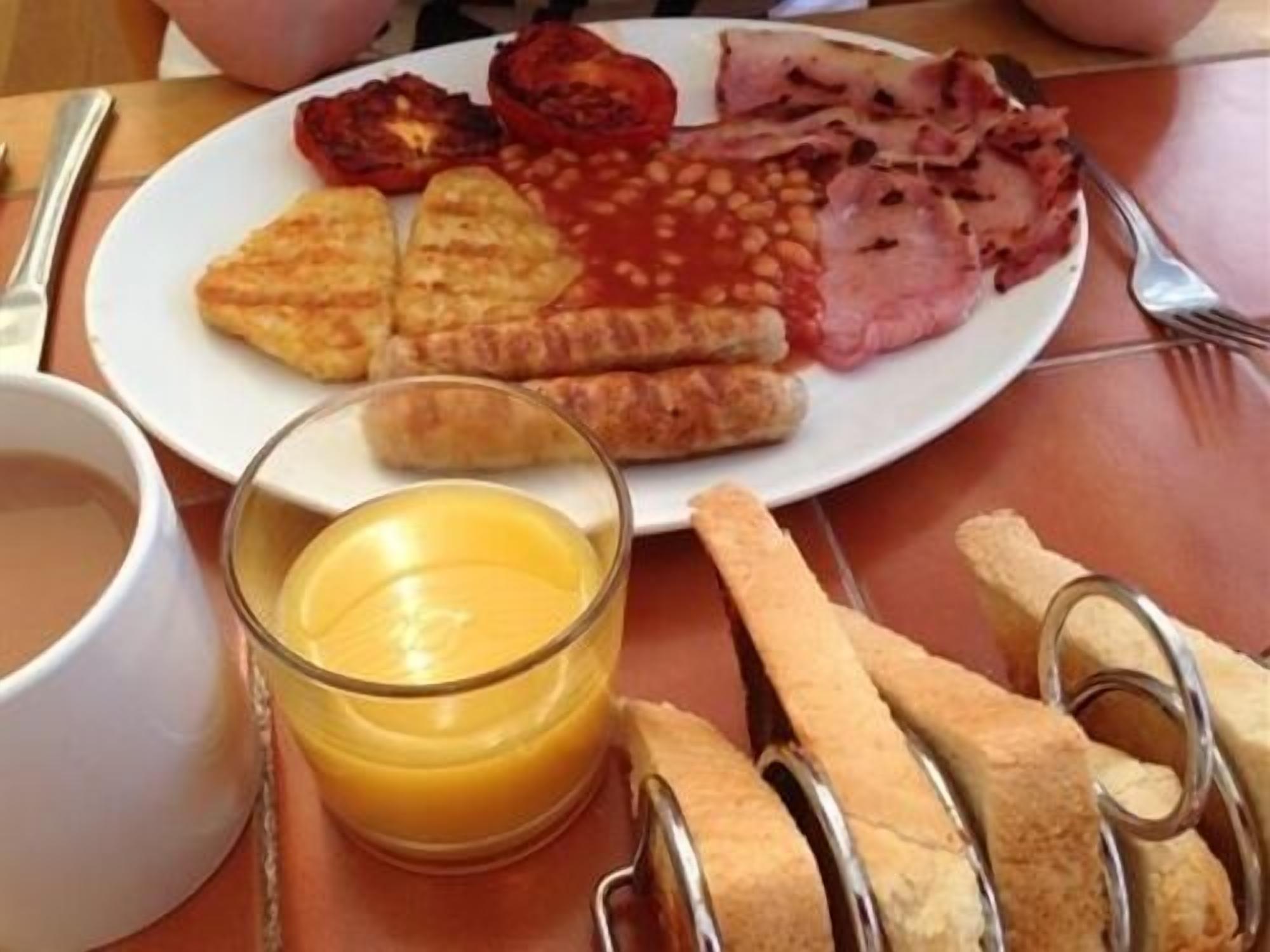 A plate with grilled tomatoes, beans, ham, and croissants, accompanied by a glass of orange juice and bread.