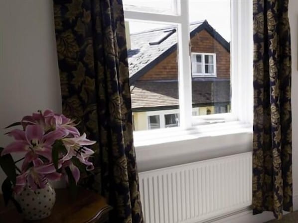 Una habitación con ventana, un jarrón con flores y un radiador.
