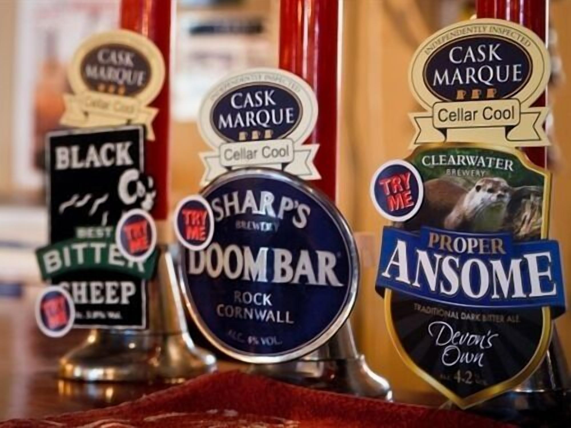 Variedad de grifos de cerveza con etiquetas que indican diferentes marcas y tipos, incluyendo 'Black Sheep', 'Sharp's Doombar' y 'Proper Ansome'.