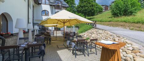 An outdoor cafe area with tables and chairs, a wooden podium, and a large umbrella.