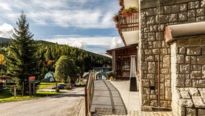 A stone building with a wooden balcony and a paved walkway leading to a road. - Wellness Hotel Windsor (Spindleruv Mlyn)