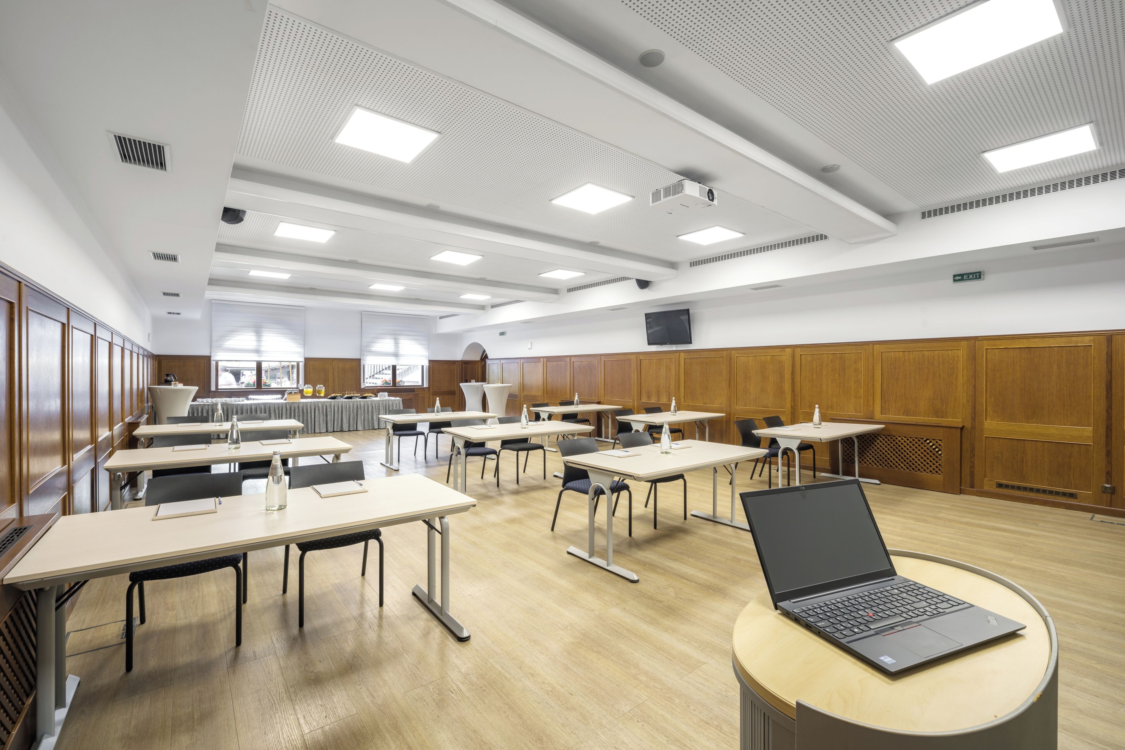 A conference room with multiple tables and chairs, a laptop on a table, and a projector on the ceiling.
