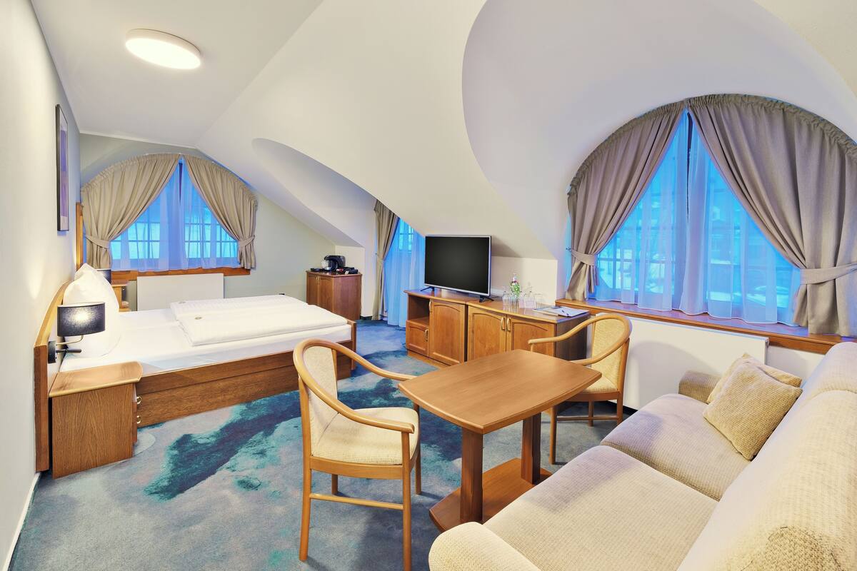 A hotel room with a bed, a desk, a TV, a sofa, and a dining table.