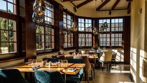 A restaurant with multiple tables and chairs, large windows, and hanging light fixtures. - Wellness Hotel Windsor (Spindleruv Mlyn)