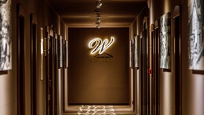 A hotel hallway with a patterned carpet, framed artwork on the walls, and a prominent illuminated 'W' sign for the Windsor Hotel. - Wellness Hotel Windsor (Spindleruv Mlyn)