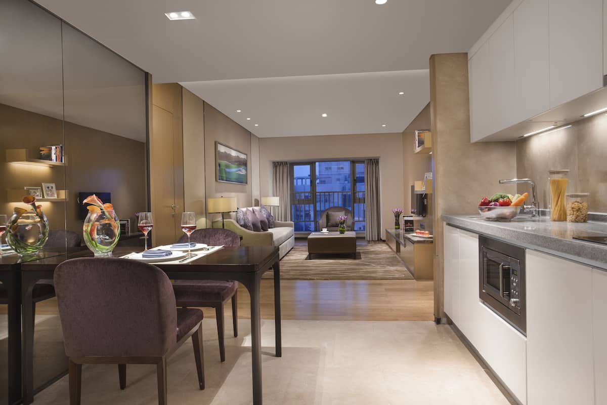 A modern hotel room with a dining area, a sofa, and a kitchen.