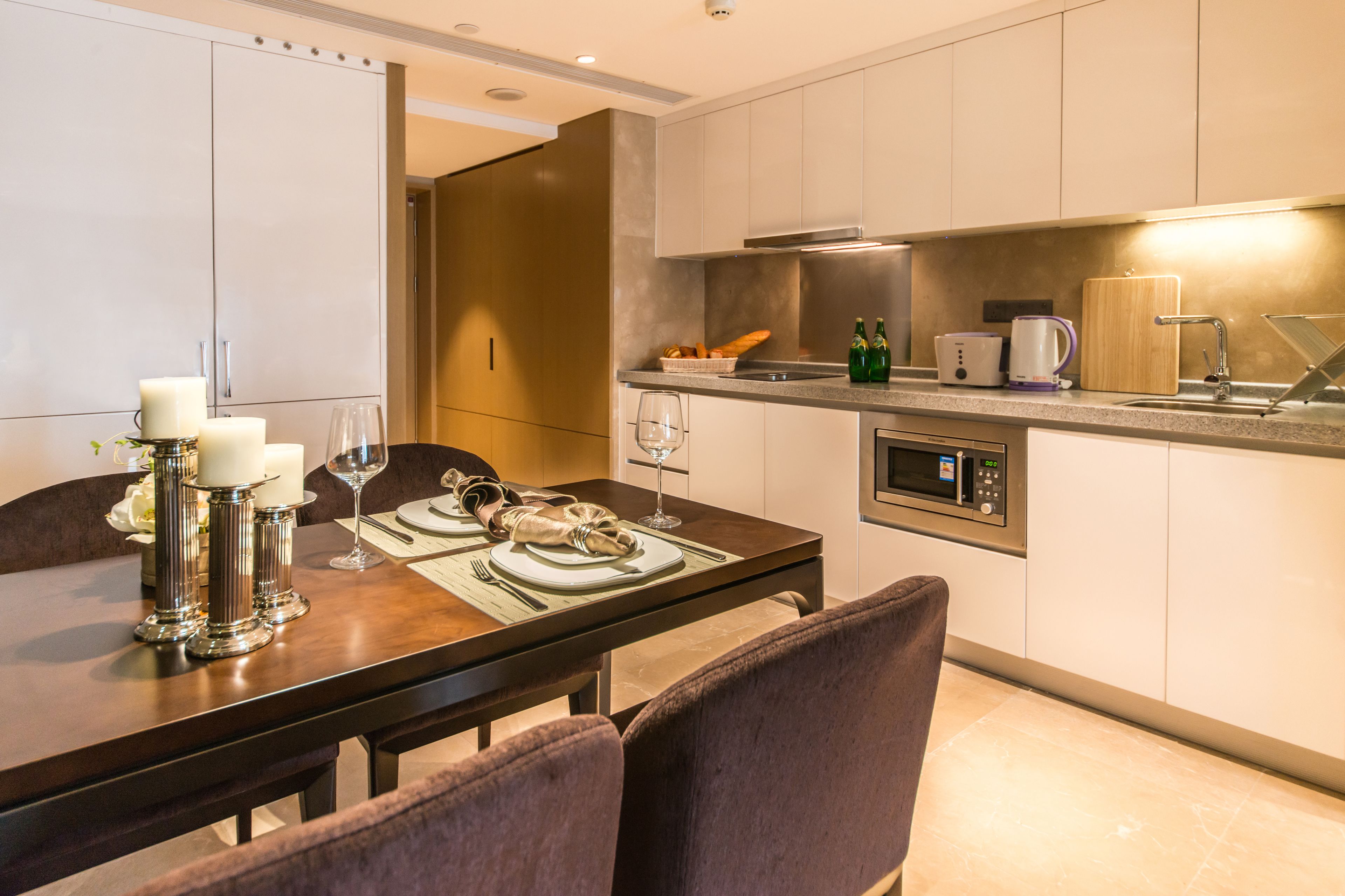 A modern kitchen with a dining area, featuring a built-in microwave, a coffee maker, and a bread basket on the counter.
